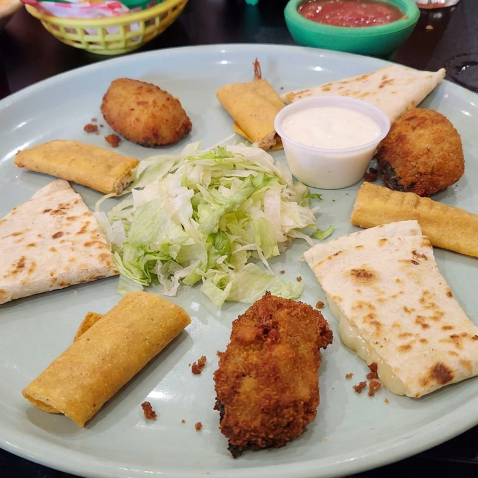 Platter of assorted fried appetizers, grilled flatbread, shredded lettuce, and dipping sauce on a restaurant table.